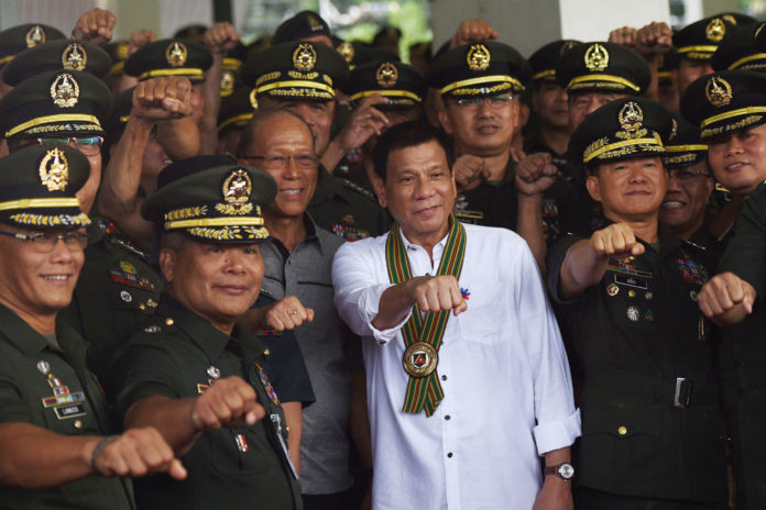 Philippine President Rodrigo Duterte (C) gestures with raised fists with military officers during a "talk to the troops" visit in Manila on October 4, 2016. Rodrigo Duterte launched a fresh tirade at the United States on October 4, telling Barack Obama to "go to hell" as the longtime allies launched war games that the firebrand Philippine leader warned could be their last. / AFP PHOTO / TED ALJIBE