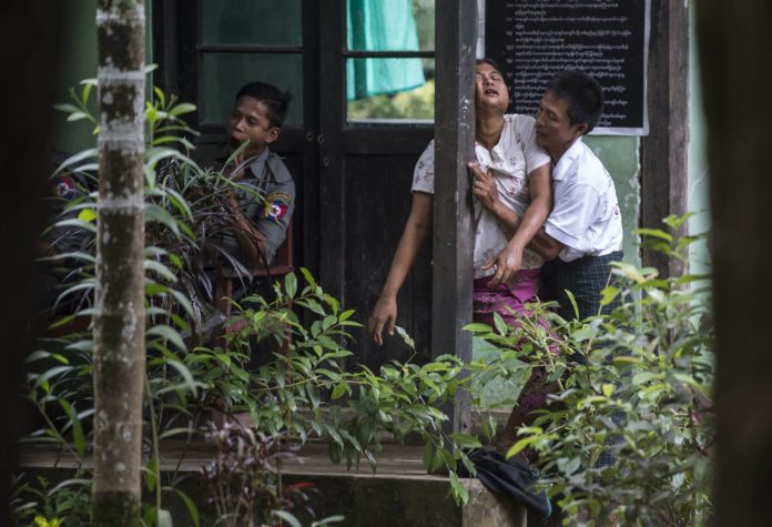 A Myanmar woman is held up by a relative as she collapses after meeting her detained brother who was facing trial, next to a yawning policeman at the courtroom entrance in Shwe Pyi Thar town on the outskirts of Yangon on October 10, 2016. / AFP PHOTO / ROMEO GACAD