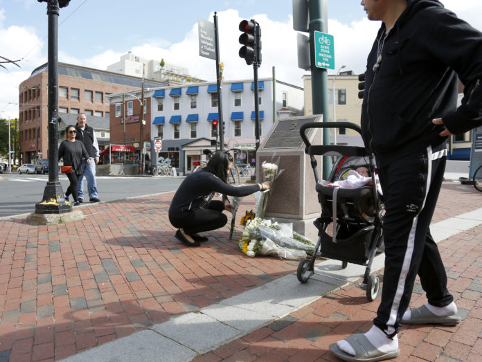 Juthamat Mongkhonlertsir, of Watertown, Massachusetts, lays flowers at a monument at King Bhumibol Adulyadej Square as her husband Teeradet waits with their infant daughter Tirada on October 13, 2016 in Cambridge, Massachusetts. Thailand's King Bhumibol Adulyadej, the world's longest-reigning monarch, has died at the age of 88, the palace announced on October 13, leaving a divided nation bereft of a rare figure of unity. / AFP PHOTO / Mary Schwalm