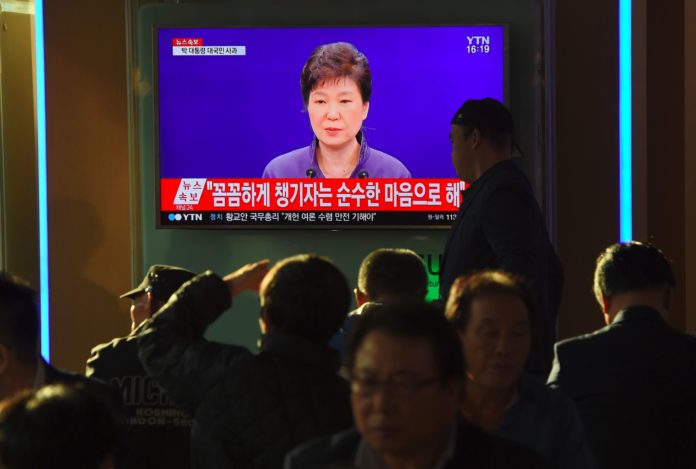 People watch a television news report showing South Korean President Park Geun-Hye making a public apology, at a railway station in Seoul on October 25, 2016. South Korean President Park Geun-Hye was forced into a public apology on October 25 for the leak of official documents to a family associate involved in a growing corruption scandal. / AFP PHOTO / JUNG YEON-JE