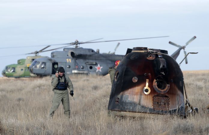 A Russian Soyuz MS space capsule rests on the ground after landing as a rescue helicopter lands nearby, about 150 kms (90 miles) southeast of the Kazakh town of Dzhezkazgan on October 30, 2016. Three astronauts landed safely in Kazakhstan on October 30 following a 115-day mission aboard the the International Space Station, including US astronaut Kate Rubins, the first person to sequence DNA in space. / AFP PHOTO / POOL / Dmitri Lovetsky