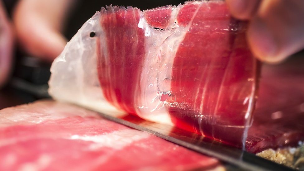 Close up of hand and knife cutting jamon iberico in Spain.