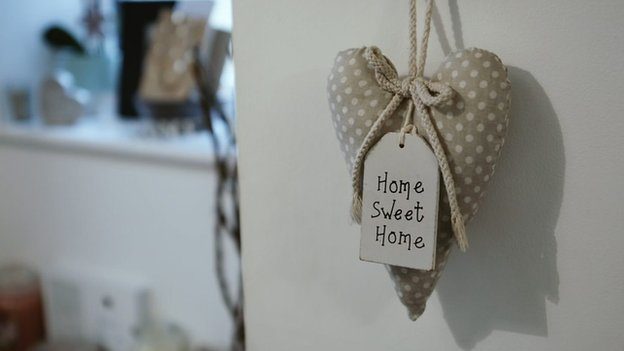 A heart-shaped trinket saying 'home sweet home' hangs from a door in Alex's family home