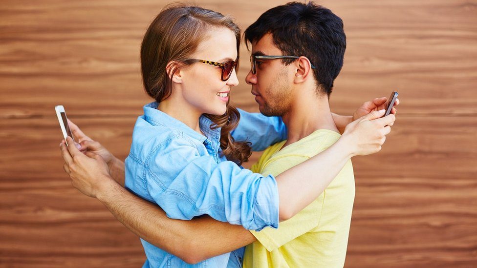 A couple embracing and texting at the same time.
