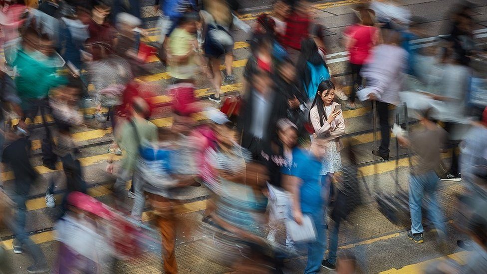 Long exposure image of Chinese businesswoman in a zebra crossing, in a very busy street with lots of people walking by, checking her mobile phone.