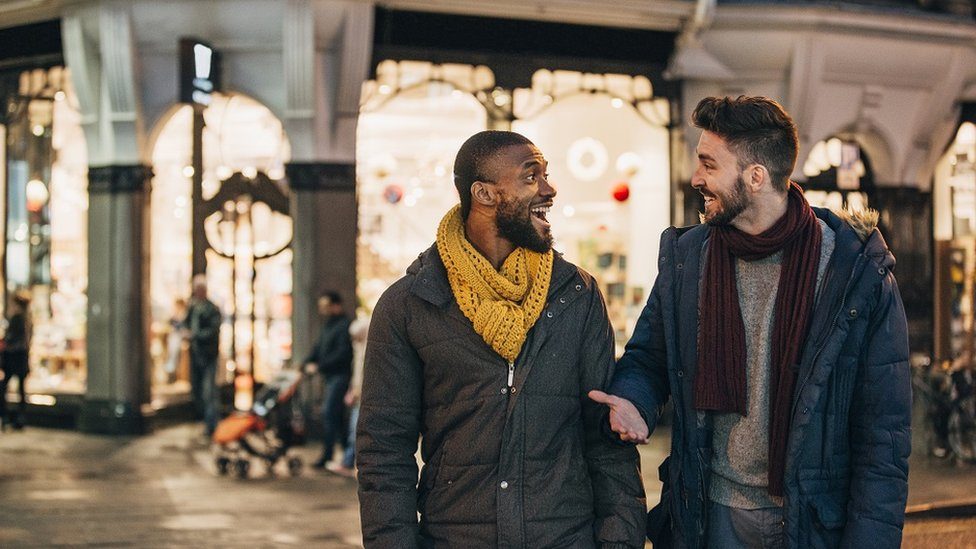 Two young men chatting happily, crossing a street in the evening