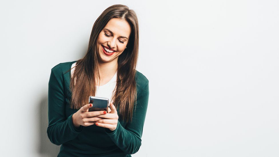A woman smiling and writing on her phone