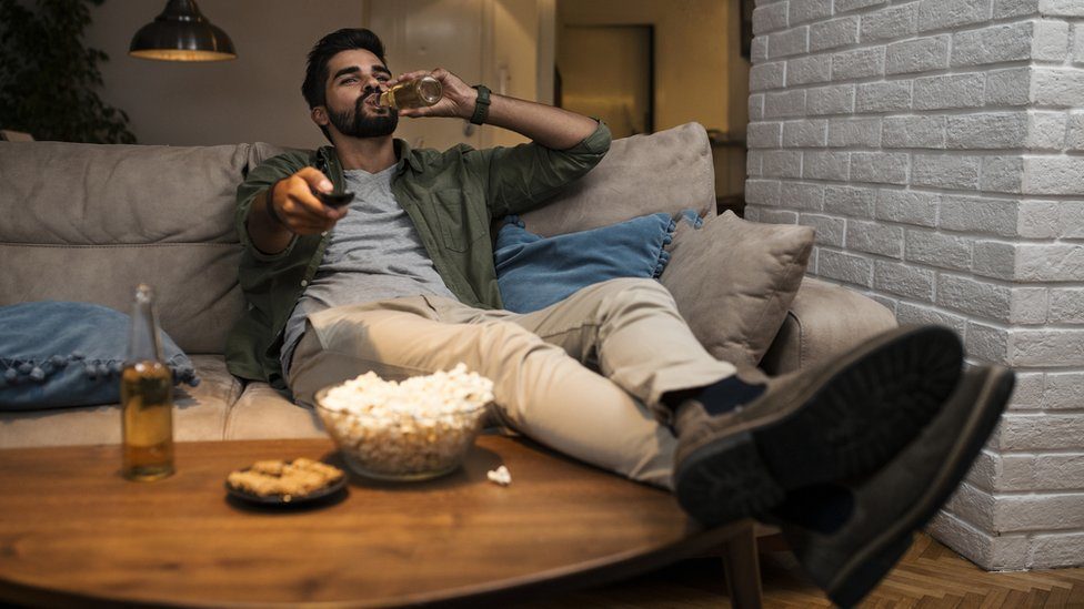 Man watching TV on sofa and having a beer