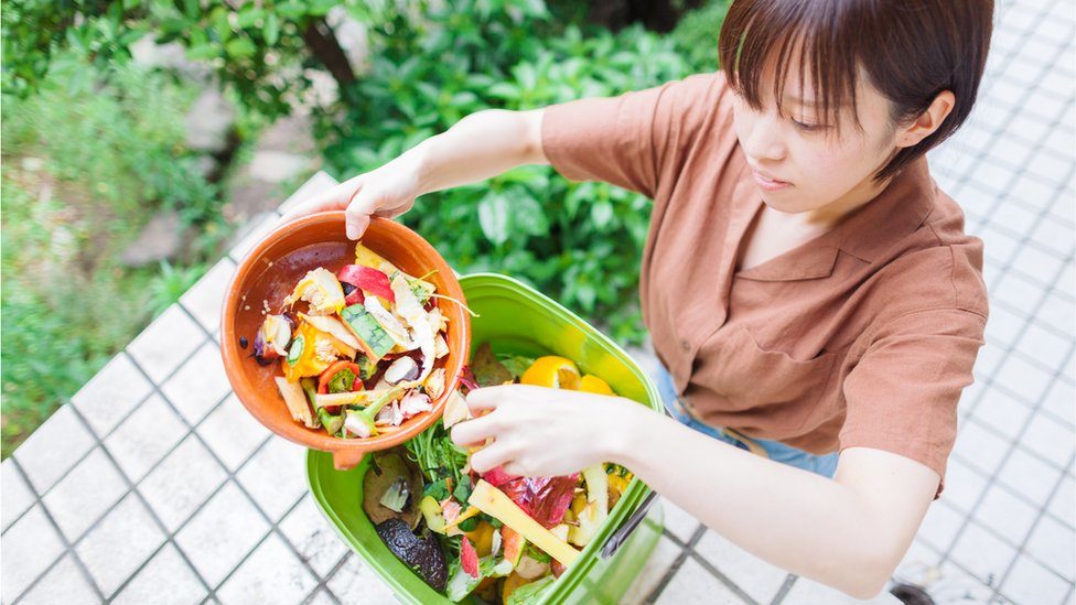 A woman throwing leftover food in a composter