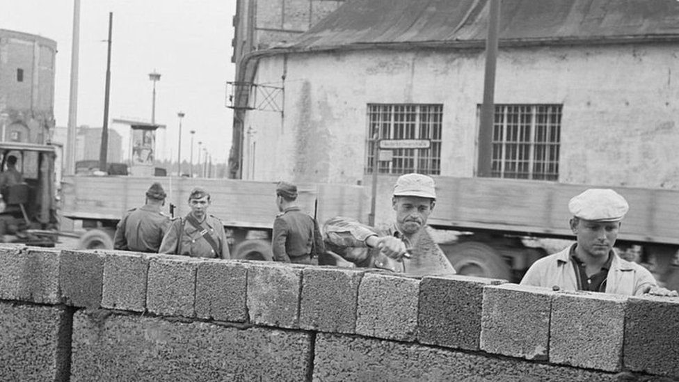 This picture shows East German workers building the Berlin wall in 1961, while being watched by communist police