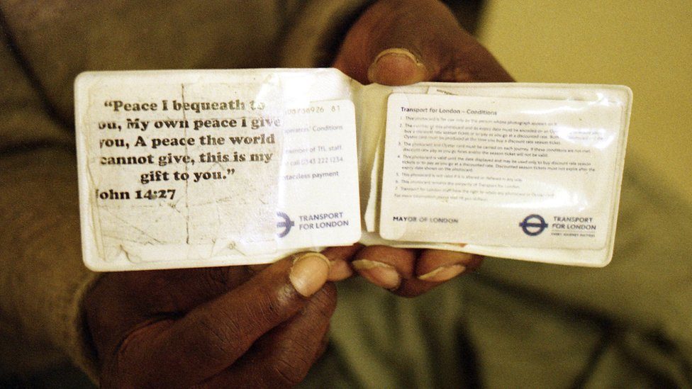 Sunny holds up his Oyster travel pass with a quotation from a Bible passage taped to the wallet
