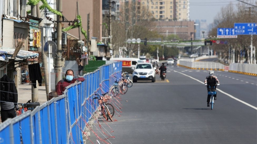 This photo taken on March 17, 2020 shows a man looking over a barrier set up to prevent people from entering or leaving a residential compound in Wuhan, in China's central Hubei province.