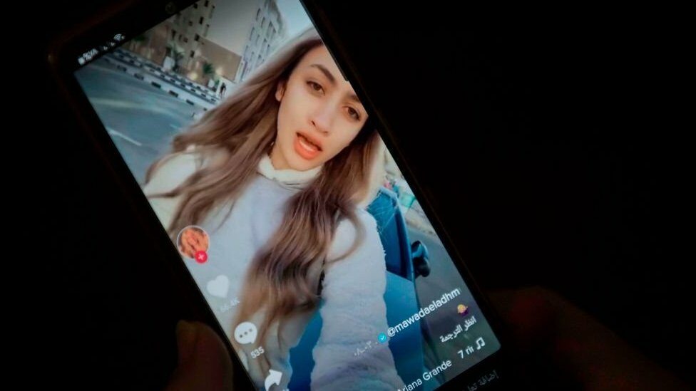 A hand holding a phone showing one of Mawada's TikTok videos in which she is lip-syncing