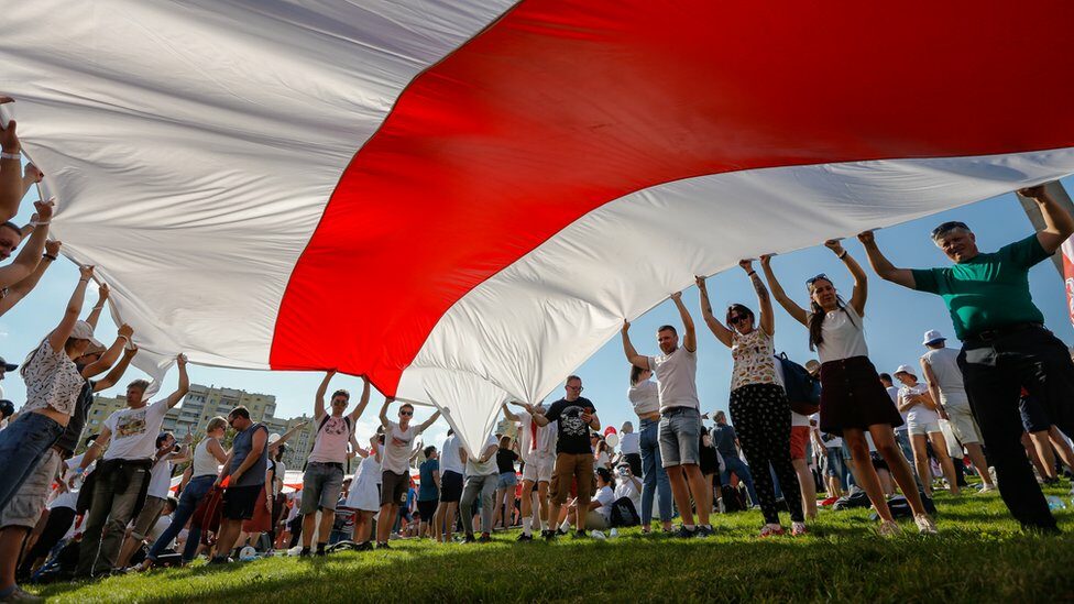 Belarusian people hold a giant historical flag of Belarus during a rally in support of the Belarusian opposition