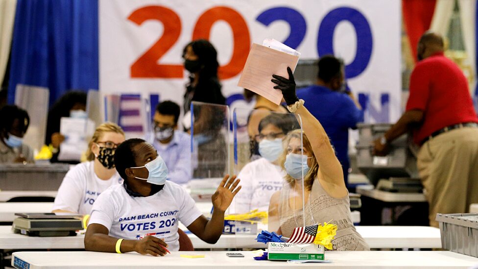 An election worker passes paper to another worker over a plastic screen