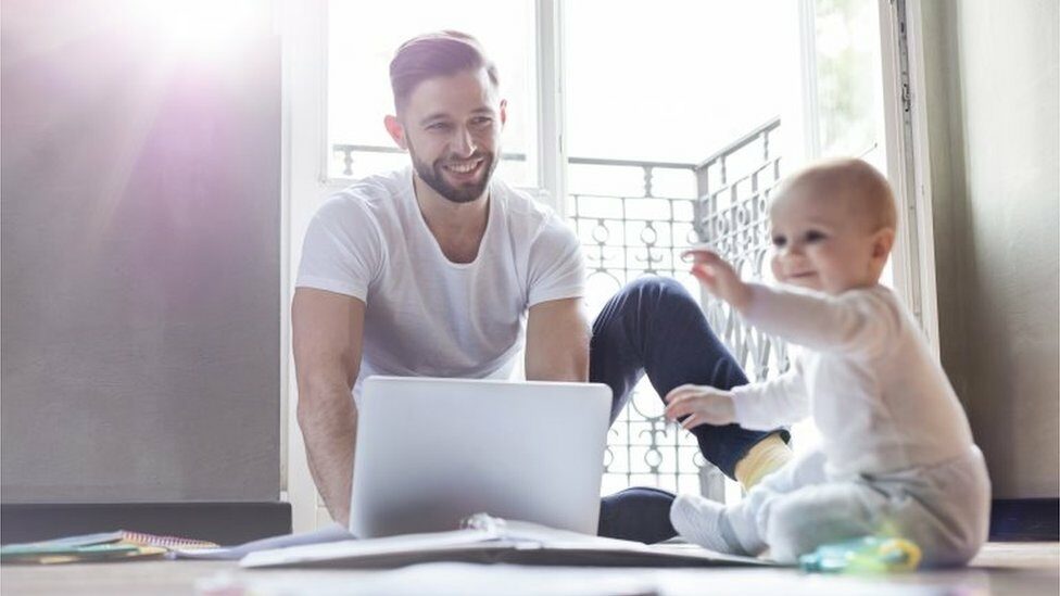 Father working on laptop and watching baby