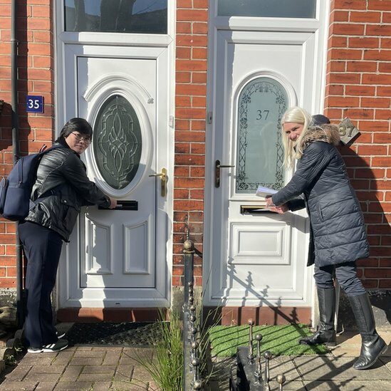Jihyun Park posts flyers through a letter box with a colleague
