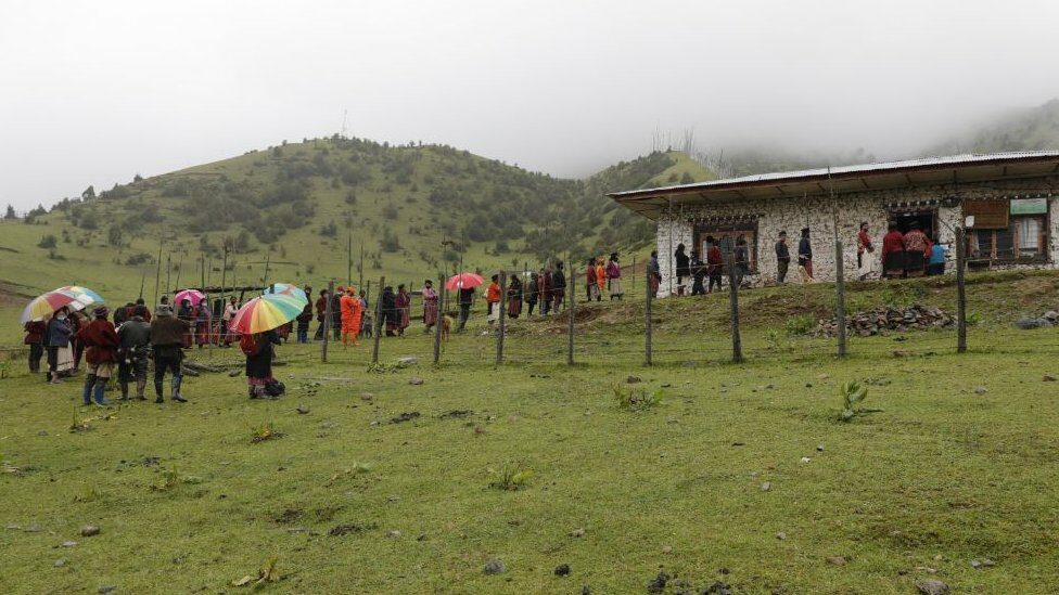 ชาวบ้านเกนกู ในเมืองทราชิกัง ทางตะวันออกของภูฏาน เข้าแถวท่ามกลางสายฝนด้านนอกศูนย์ชุมชน