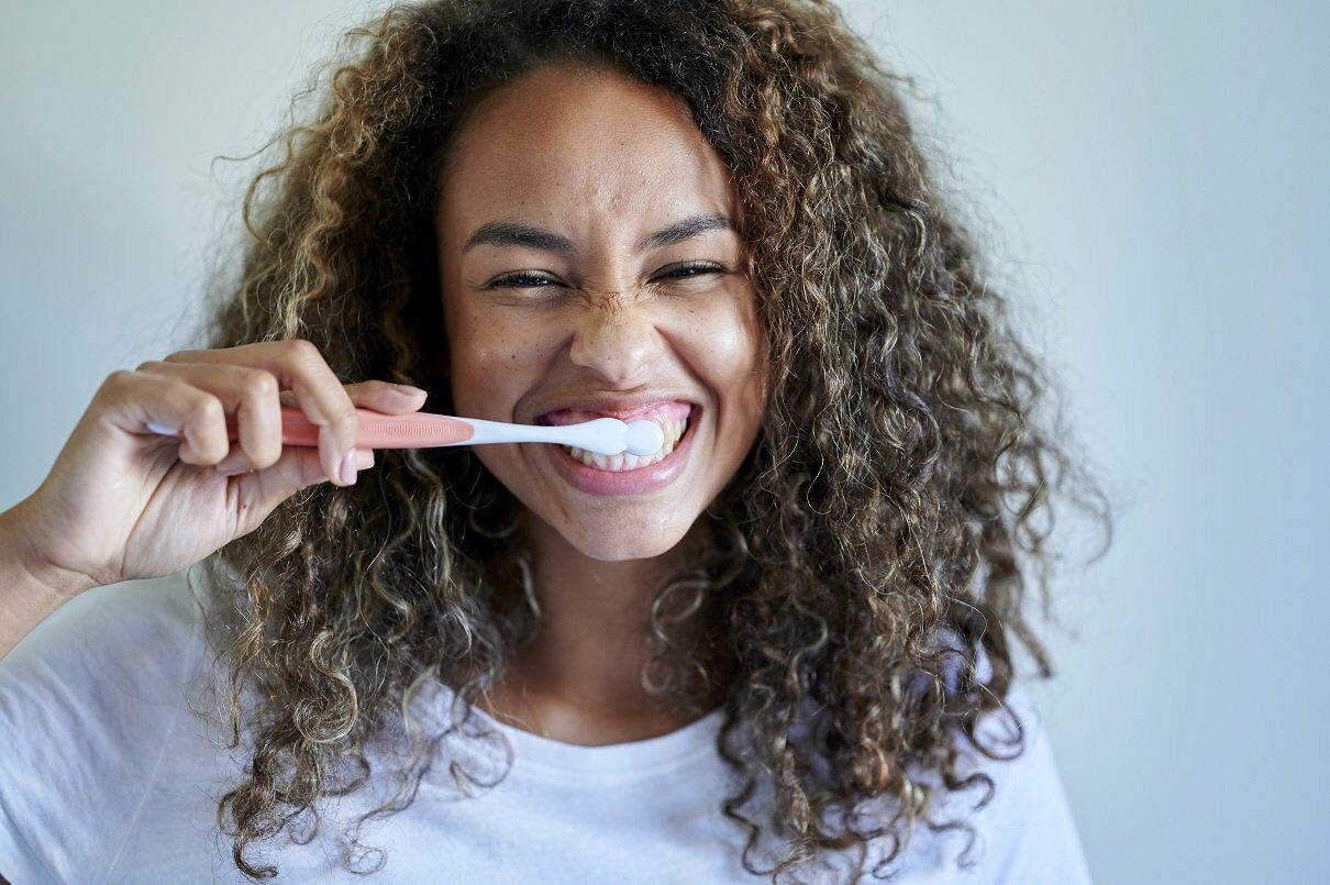 Cheerful young woman enjoying while brushing teeth against wall