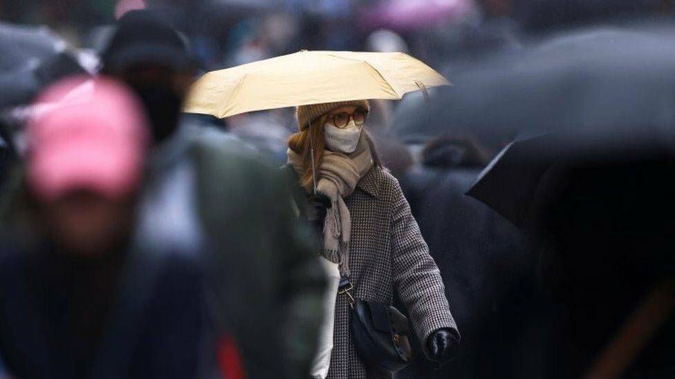 A woman, wearing a protective mask, holds an umbrella while she walks on Montorgueil street in Paris amid the coronavirus disease (COVID-19) outbreak in France, December 3, 2021.