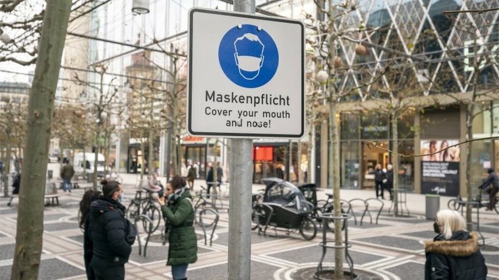 A sign reading "Cover your mouth and face" stands at the Zeil shopping street in downtown Frankfurt am Main, Germany, 11 January 2022.
