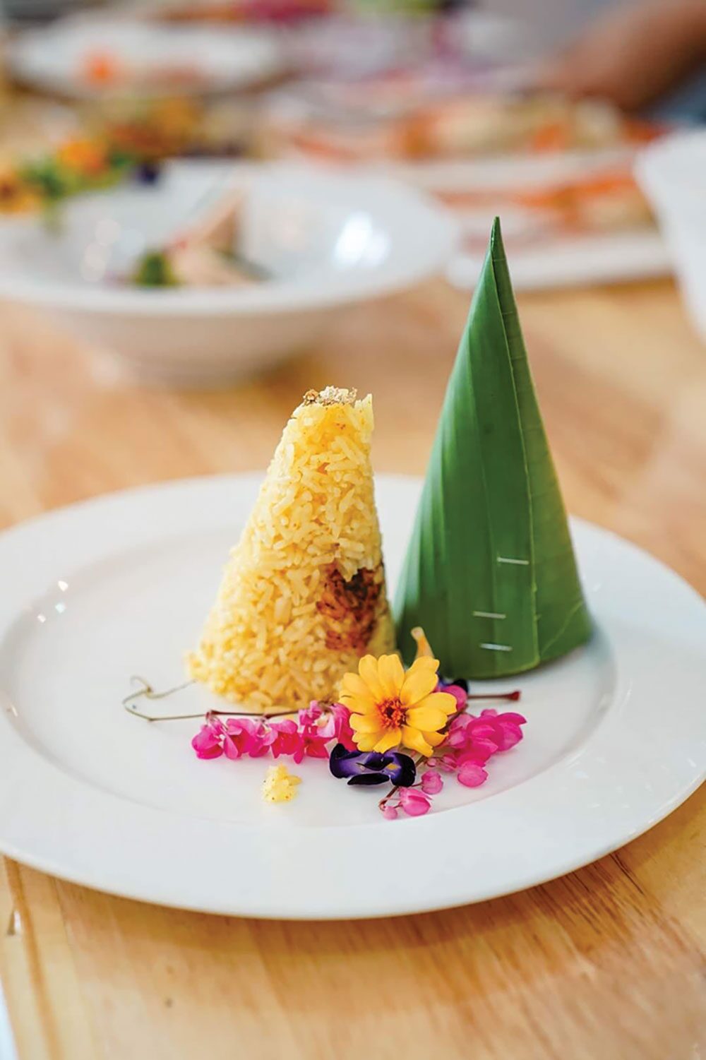  หากกล่าวถึง ร้านอาหารสไตล์เชฟเทเบิล หลายคนคงจะนึกถึงเมนูอาหารญี่ปุ่น หรืออาหารสไตล์ยุโรปสุดหรู ที่รังสรรค์โดยเชฟมากฝีมือที่มาในราคาแพงหูฉี่  แต่สำหรับ ‘ร้านขนมอมยิ้ม’ กาญจนบุรี เป็นร้านอาหารไทยสไตล์เชฟเทเบิล ร้านแรกและร้านเดียวในจ.กาญจนบุรี มี เชฟแมนนี่ ผู้ซึ่งมีความเชี่ยวชาญด้านอาหารไทยและขนมไทย รับหน้าที่เป็นทั้งเจ้าของร้านและเชฟประจำร้าน