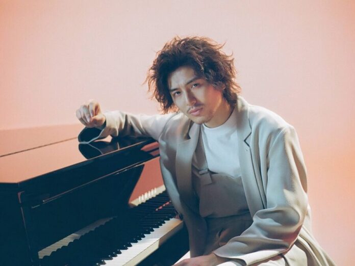 ผู้ชายผมยาวไว้หนวด นั่งเท้าแขนบนเปียโนสีดำ