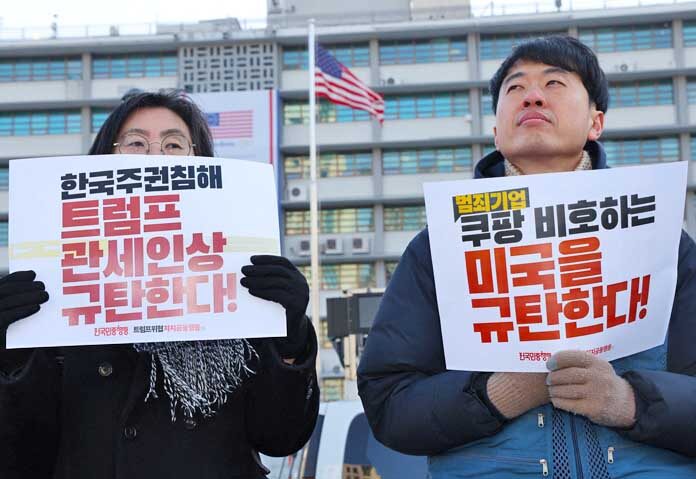 กลุ่มนักกิจกรรมถือป้ายที่มีข้อความว่า "ประณามการละเมิดอธิปไตยของเกาหลีใต้และนโยบายภาษีของทรัมป์!" และ "ประณามสหรัฐอเมริกาที่ปกป้องบริษัทคูปัง!" ระหว่างการชุมนุมต่อต้านทรัมป์หน้าสถานทูตสหรัฐฯ ในกรุงโซล ประเทศเกาหลีใต้ เมื่อวันที่ 27 มกราคม 2569