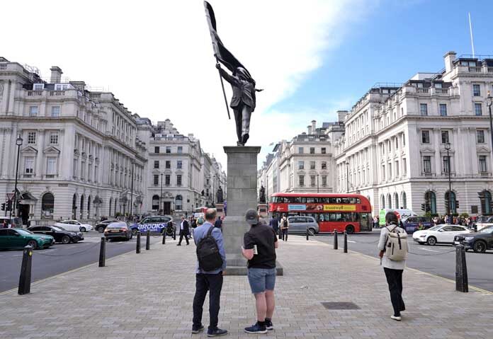 ประชาชนกำลังชมรูปปั้นชายคนหนึ่งถือธงปิดบังใบหน้า ซึ่งมีลายเซ็น "Banksy" ปรากฏอยู่ที่จัตุรัสวอเตอร์ลูในลอนดอน