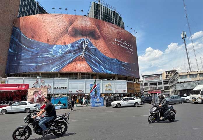 ทรัมป์กล่าวหาอิหร่าน - รถยนต์ขับผ่านป้ายโฆษณาที่มีภาพกราฟิกแสดงช่องแคบฮอร์มุซและริมฝีปากที่เย็บของประธานาธิบดีโดนัลด์ ทรัมป์ แห่งสหรัฐอเมริกา ในจัตุรัสใจกลางกรุงเตหะราน ประเทศอิหร่าน เมื่อวันเสาร์ที่ 2 พฤษภาคม 2569
