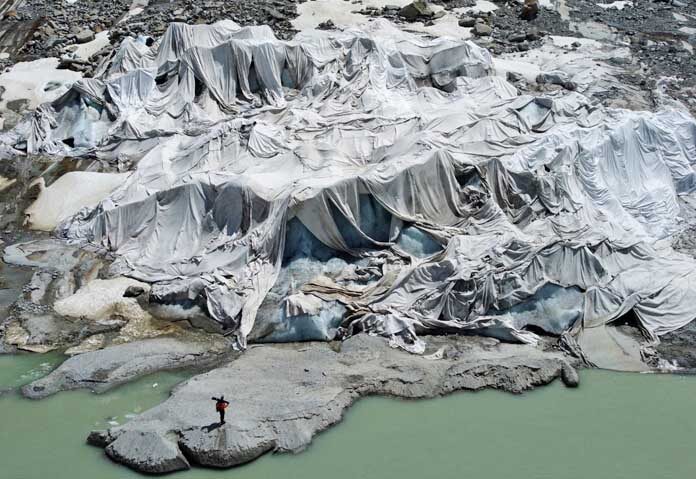 ภาพแฟ้มข่าว — ธารน้ำแข็งโรน (Rhone Glacier) ใกล้เมืองกอมส์ ประเทศสวิตเซอร์แลนด์ บางส่วนถูกคลุมด้วยแผ่นวัสดุ โดยมี Matthias Huss หัวหน้ากลุ่ม GLAMOS ซึ่งทำหน้าที่ติดตามสถานะธารน้ำแข็งของสวิตเซอร์แลนด์ ยืนอยู่ใกล้ๆ เมื่อวันที่ 10 มิถุนายน 2025